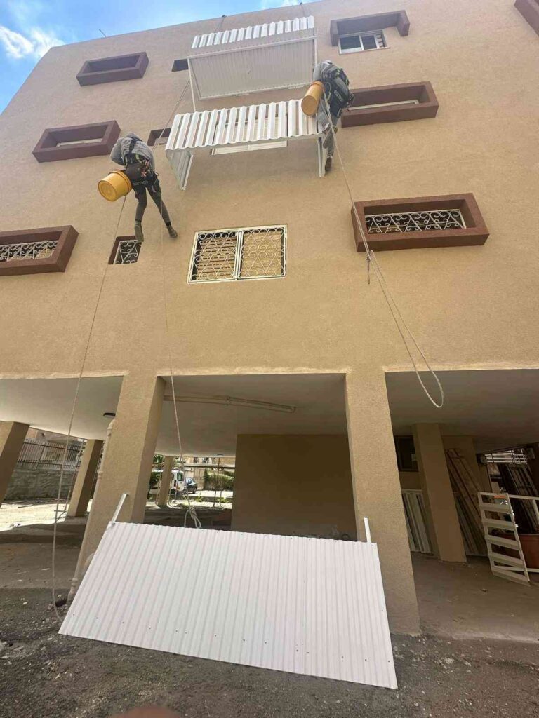 עובד מבצע עבודות סנפלינג בגובה על חזית בניין לצורך תחזוקה ותיקון קירות חוץ.
